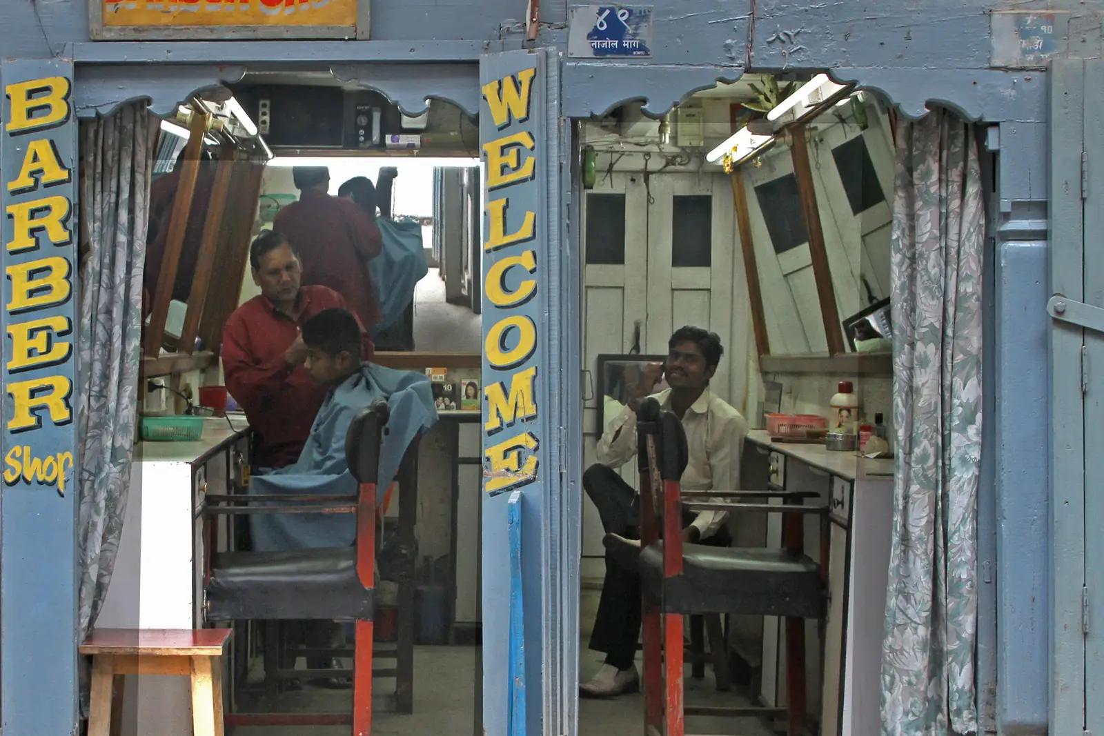 A barber cutting a customer's hair inside a small barber shop in Kathmandu, seen through the open doorway